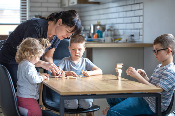 Małe dzieci grać w grę planszową z drewnianymi kostkami w domu w kuchni z mamą. - Zdjęcie, obraz
