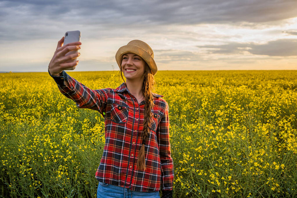 Proud female farmer is taking selfie in front of her rapeseed field. - Photo, Image