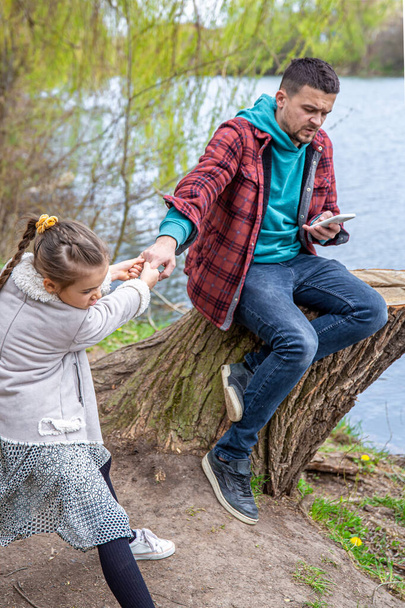 The little girl pulls dad out for a walk, but he checks his phone and pays no attention. - Photo, Image