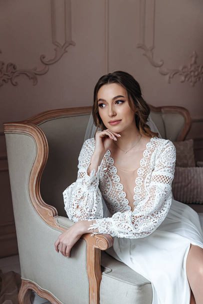 Pensive bride posing in an armchair in a boho style wedding dress. Wedding photo session, bride's morning. - Photo, Image