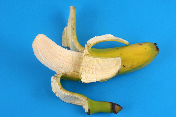 青い背景に半皮のバナナのクローズアップ - 写真・画像