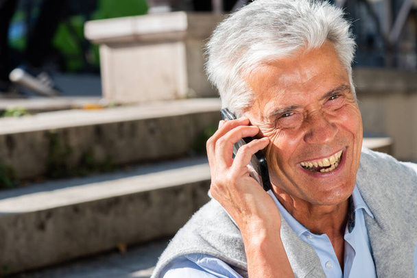 Nahaufnahme des horizontalen Porträts eines lächelnden alten Mannes, der mit seinem Mobiltelefon spricht - Foto, Bild
