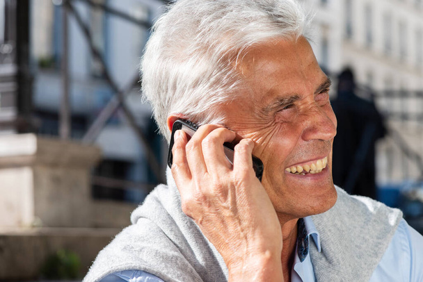 Retrato de cerca de un hombre mayor sonriente hablando con un celular afuera - Foto, imagen