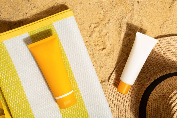 Orange and white tubes of sunscreen on beach next to straw hat and mat. Sun protection on vacation. Top view - Foto, imagen