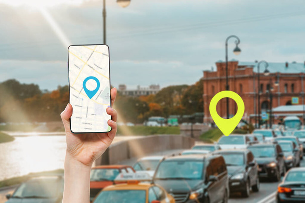 Naisen kädessä on älypuhelin, jossa on online-karttasovellus. Taustalla on kaupungin katu, jossa on liikenneruuhka ja sijainnin kuva.Käsite online-navigointi ja GPS. - Valokuva, kuva