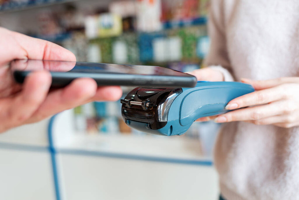 Myyjällä on maksupääte, ja mies maksaa ostoksen älypuhelimella verkossa. Sivunäkymä NFC konsepti, liiketoiminta ja pankkitoiminta. - Valokuva, kuva