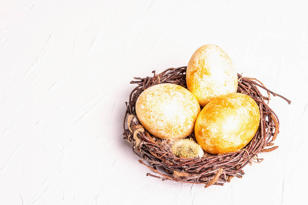 Kultaisia pääsiäismunia pajupesässä. Perinteinen pääsiäinen symboli, juhlava sisustus. Valkoinen kipsi tausta, kopioi tilaa - Valokuva, kuva