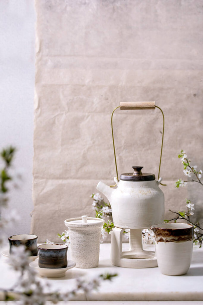 White and black craft handmade ceramic teapot with black ceramic mugs, katakuchi jug and blossoming cherry tree as decoration standing on marble table. Traditional Japanese tea ceremony. Teadrinking - Foto, Imagem