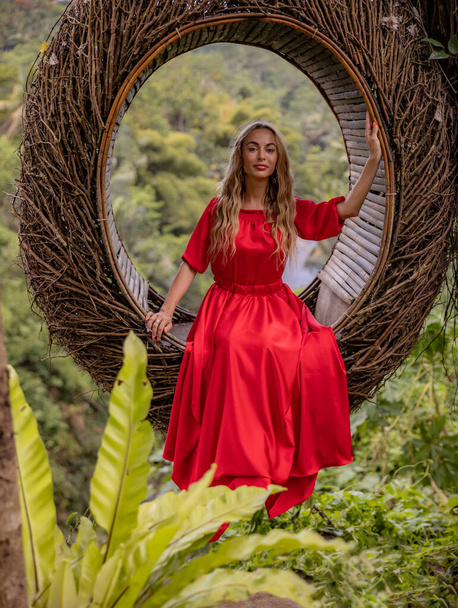 Bali trend. Straw nest in tropical forest. Caucasian woman in long red dress taking photo in a straw nest. Vacation in Asia. Travel lifestyle. Summer concept. Bongkasa, Bali, Indonesia - Photo, Image