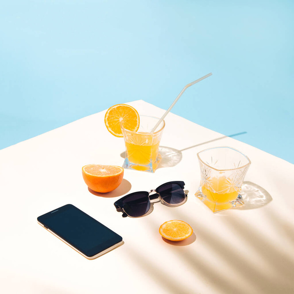 Summer tropical composition with palm leaf shade. Yellow smoked orange juice on the table with glasses and a surf phone. Holidays in a cafe. - Photo, image