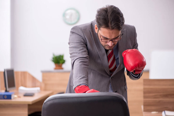 Young male employee wearing boxing gloves at workplace - Фото, зображення