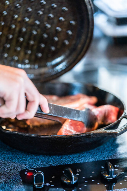 Frying New York strip steak in cast iron frying pan over the electric stove. - Fotoğraf, Görsel