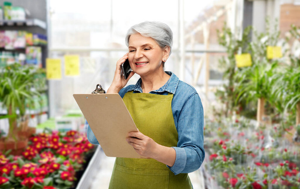 old female gardener with clipboard calls on phone - Foto, afbeelding