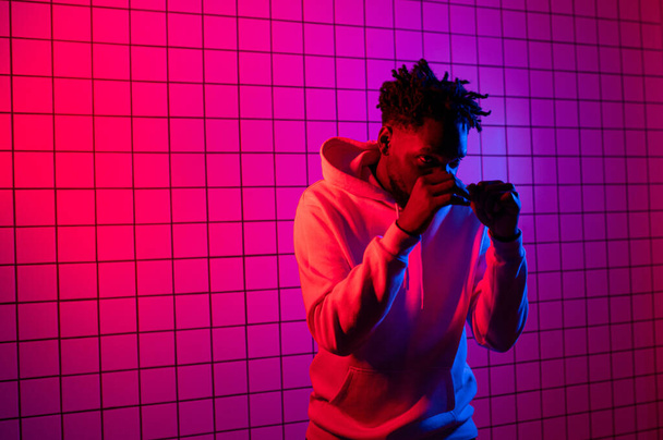 Portrait of an African American man in a hoodie on a neon background. Red-blue background. - 写真・画像