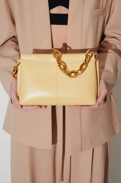 Girl in beautiful beige suit with luxury yellow leather handbag in her hands with massive gold chain. Vertical fashion photo. Closeup. Shopping concept photo. Free space for logo or advert. - Φωτογραφία, εικόνα