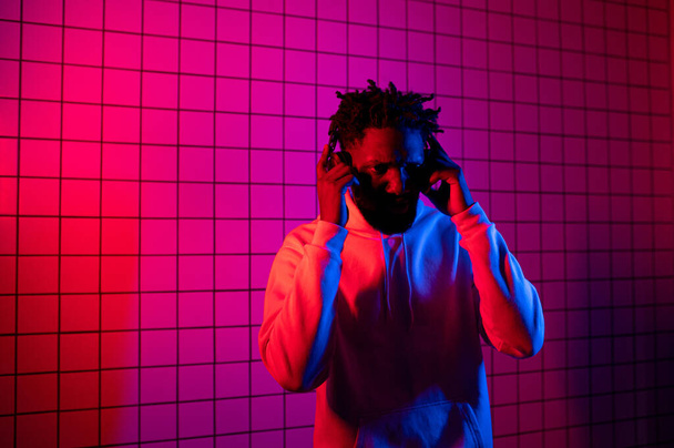 the concept of music. A black man listens to music with headphones on against a background of neon light. Red and blue background - Photo, image