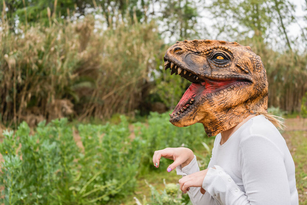 Vista da vicino della donna con la maschera della testa di dinosauro nel giardino delle verdure. - Foto, immagini