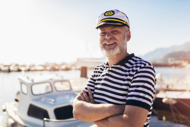 Uomo maturo in piedi vicino al mare vestito con camicia e cappello da marinaio. - Foto, immagini