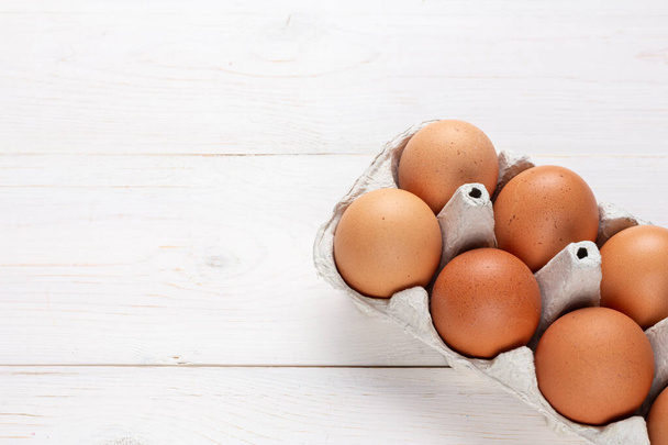 Fresh organic chicken eggs in carton pack or egg container  on white wood background. Space for text. - Photo, image