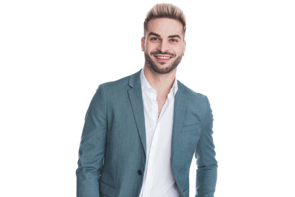 portret szczęśliwego młodego biznesmena w garniturze z rozwiązaną koszulą uśmiecha się i pozowanie odizolowany na białym tle w studio - Zdjęcie, obraz