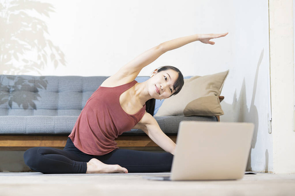 Uma mulher fazendo ioga enquanto olha para a tela do computador na sala - Foto, Imagem