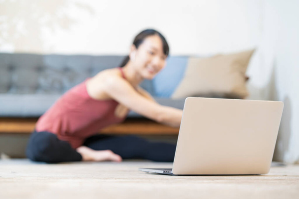 Out-of-focus schieten van een vrouw die yoga terwijl het kijken naar het scherm van een laptop computer - Foto, afbeelding
