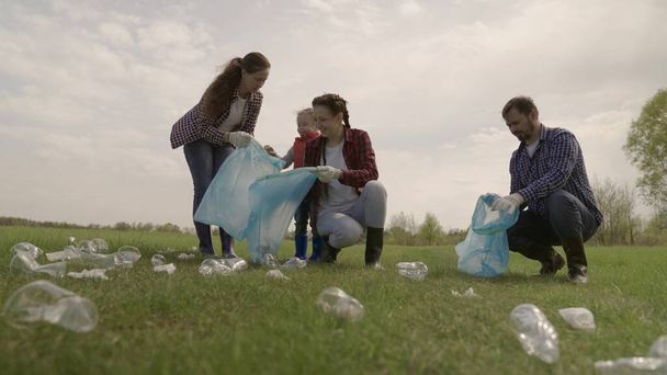 Ένα μικρό παιδί με τους γονείς του συλλέγει σκουπίδια σε έναν χώρο αναψυχής του πάρκου, ομαδικό καθαρισμό της περιοχής, οικολογία της καθαριότητας, συλλογή πλαστικών μπουκαλιών, απόβλητα, ομαδική εργασία, ευτυχισμένη οικογένεια και παιδί - Φωτογραφία, εικόνα