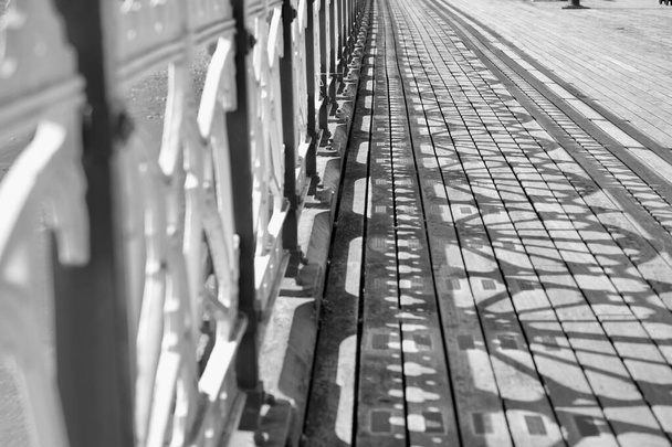 Monochrome foto van oude Victoriaanse pier en promenade. Het zonlicht stroomt door de ingewikkelde ontwerpen en creëert schaduwpatronen op de houten promenade - Foto, afbeelding