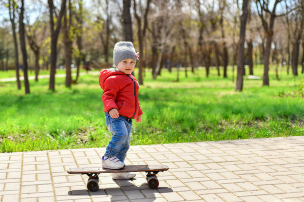 A little girl is riding a skateboard on the sidewalk path in the park. - Foto, afbeelding