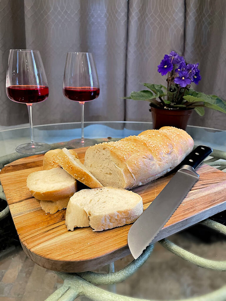 Pan de sémola hecho en casa en rodajas y listo para servir con dos copas de vino y una flor violeta africana en el fondo. - Foto, imagen