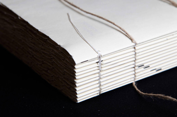 Het proces van boekbinden; het sluiten van een rauw boek na het naaien van koorden. Zwarte achtergrond - Foto, afbeelding
