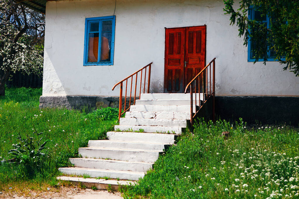 Casa con porta rossa e scala bianca. Casa in villaggio con pareti dipinte di bianco. Vecchia casa rustica - Foto, immagini