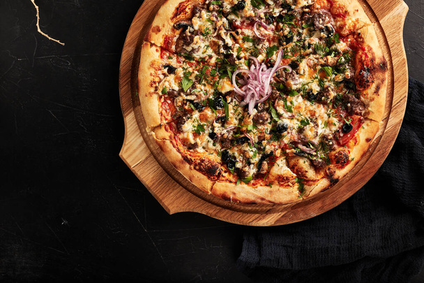 pizza sobre una base de madera sobre un fondo negro con textura vista superior - Foto, imagen