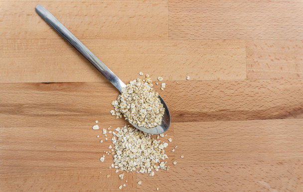 Stockholm, Sweden - May 9, 2021: Isolated spoon with rolled oats on wooden background and with a heap of oats - Photo, Image