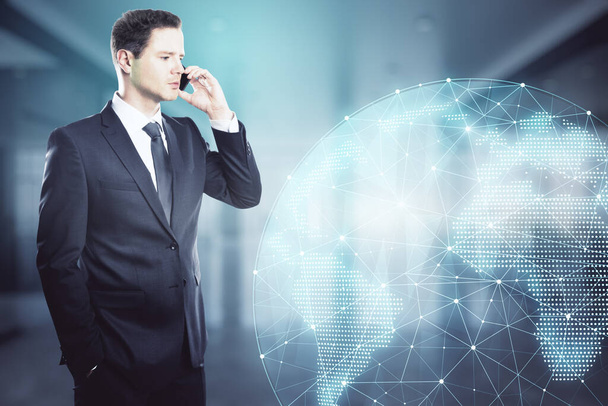 Businessman talking on the phone in an office with big windows and a holographic globe in the background, global communication and social network concept - Foto, Bild