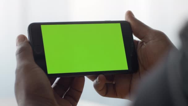 Мобильный телевизор. Закрыть снимок смартфона с экраном зеленой хромированной клавиши в черных мужских руках, мужчина смотрит видео онлайн - Кадры, видео