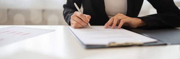 Wide view closeup image of a businesswoman signing a document or application form in a folder. - Фото, изображение