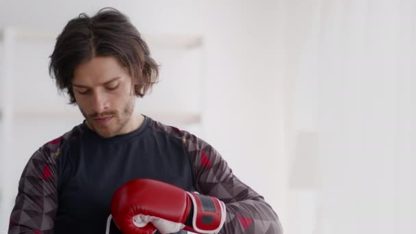Nuori aktiivinen kaveri laittaa punainen nyrkkeily käsineet, valmistautuu aloittamaan itsepuolustusta harjoitus, törmäävät nyrkit, seuranta laukaus - Materiaali, video