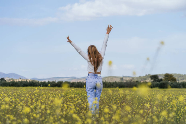 Молодая женщина счастливо позирует на поле желтых цветов - Фото, изображение