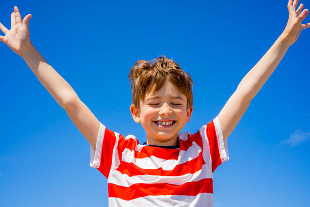Šťastný chlapec zvedá ruce nad modrou oblohu. Cítit svobodu, užívat si života a přírody. Koncept letních prázdnin.  - Fotografie, Obrázek