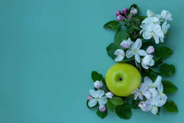 Trend lay-out met takken van een bloeiende boom en verse appel op een groene achtergrond. Bloemen en fruit samenstelling. Minimaal voorjaarsconcept. Vlakke lay met kopieerruimte. - Foto, afbeelding