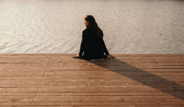 Lonely woman sitting on pier near river - Фото, изображение