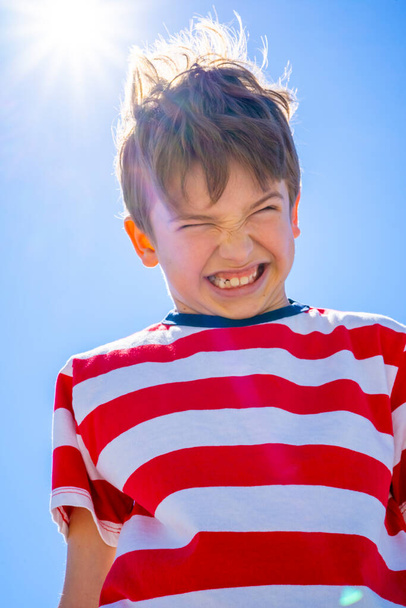 Vzteklý emocionální chlapec nad modrou oblohou se sluncem. Rozrušený chlapecký koncept. Kvalitní fotografie - Fotografie, Obrázek