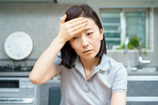 Asijské středního věku žena trpí bolestí hlavy v místnosti - Fotografie, Obrázek