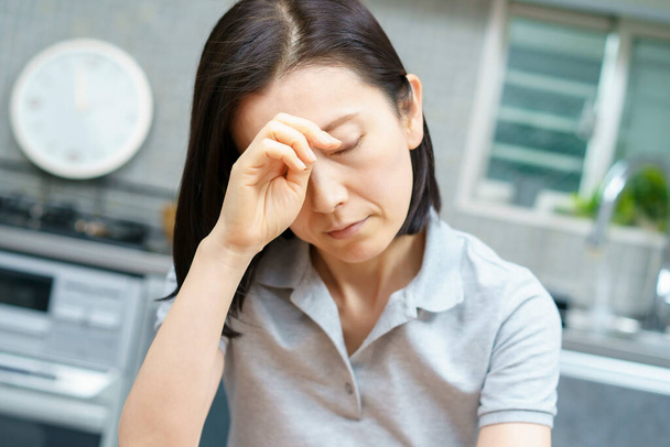 Asiatische Frau mittleren Alters leidet unter Kopfschmerzen im Zimmer - Foto, Bild