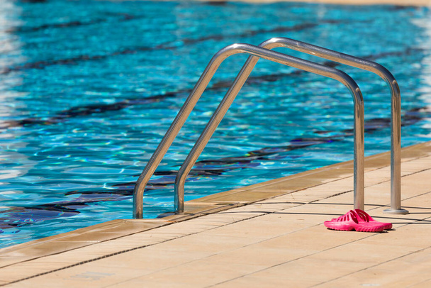 Tongs roses, à côté des échelles d'accès à l'eau, en acier inoxydable, situées sur le bord d'une piscine dans la municipalité de Gallur, Aragon, Espagne, par une journée d'été ensoleillée. - Photo, image