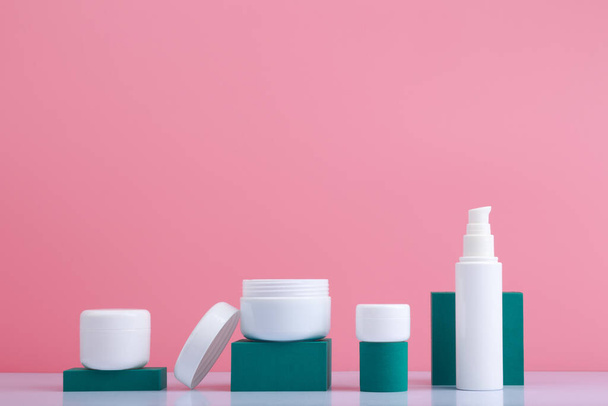Variedade de produtos de cuidados com a pele com suportes geométricos verdes contra fundo rosa com espaço de cópia - Foto, Imagem