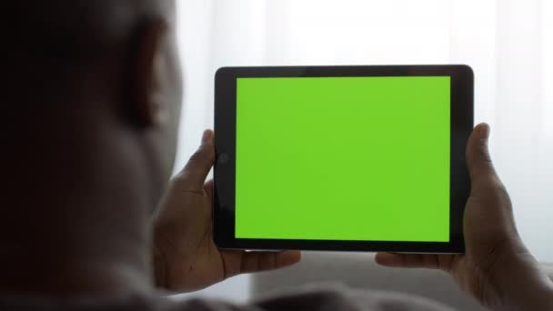 デジタルテレビ。緑のクロマキー画面でデジタルタブレットでビデオを見ているアフリカ系アメリカ人男性のクローズアップ,モックアップ - 映像、動画