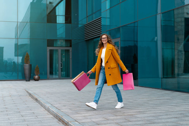 Business Woman With Shopping Bags Dressed Yellow Coat Walking Outdoors Corporative Building Background Caucasian Female Business Person Office Building Stylish Businesswoman Season Sale full length - Foto, Imagem