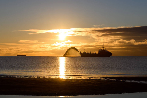 Σκάφος που συμμετέχει σε βυθοκόρηση το ηλιοβασίλεμα. Ο Χόπερ Ντρέντζερ δουλεύει στη θάλασσα. Σκάφος που σκάβει υλικό από υδάτινο περιβάλλον. Όμορφο ηλιοβασίλεμα. - Φωτογραφία, εικόνα